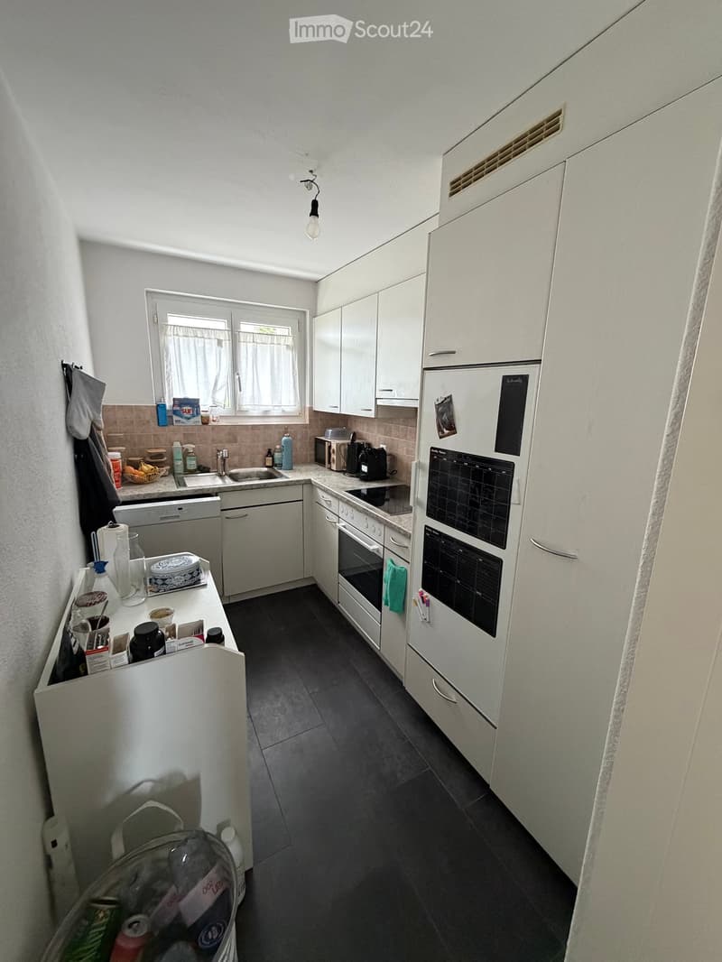 Modern kitchen with white cabinets, stainless steel appliances, and a dark tiled floor. Features include a refrigerator, oven, dishwasher, sink, and various kitchen items on the counter.
