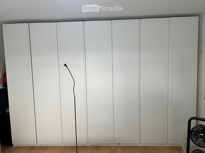Empty room with white built-in wardrobes, wooden floor, and a small fan visible in the corner.