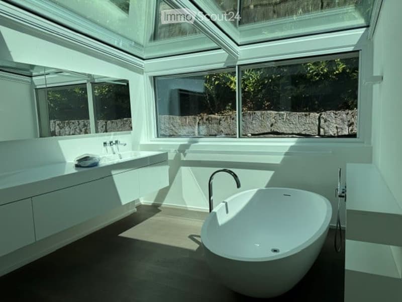 Modern bathroom with a large, freestanding bathtub, a sleek sink, and large windows offering natural light and a view of greenery outside.
