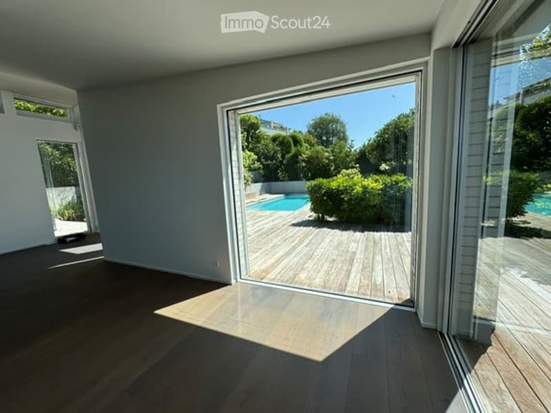 Bright, unfurnished room with large sliding glass doors opening to a wooden deck and a swimming pool area.