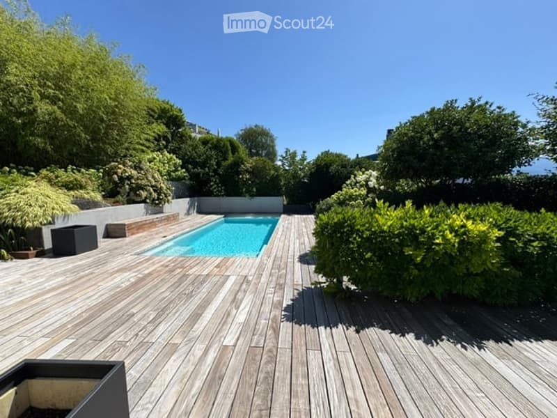 Wooden deck patio with a swimming pool, surrounded by lush greenery and trees.
