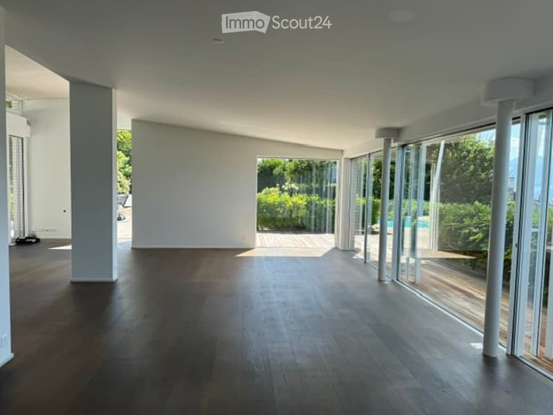 Open, unfurnished room with wooden flooring, large glass walls, and a view of a swimming pool and greenery outside.