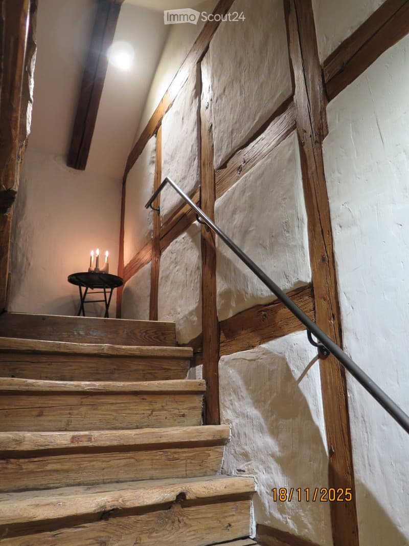 Wooden staircase with metal railing, stone walls, small table with candles on landing.