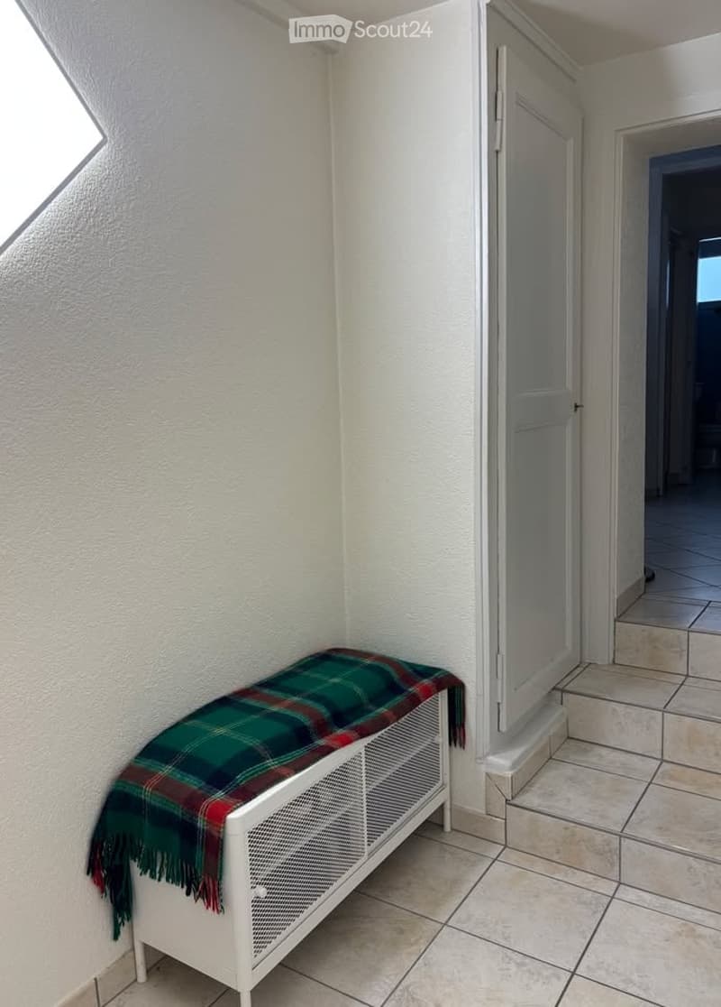 A small hallway with a white bench covered in a green and red plaid blanket, adjacent to a doorway leading to another room.