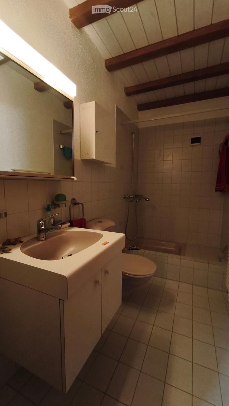 Bathroom with a sink, toilet, bathtub, mirror, and cabinet. The room features tiled walls and floor, with wooden beams on the ceiling.