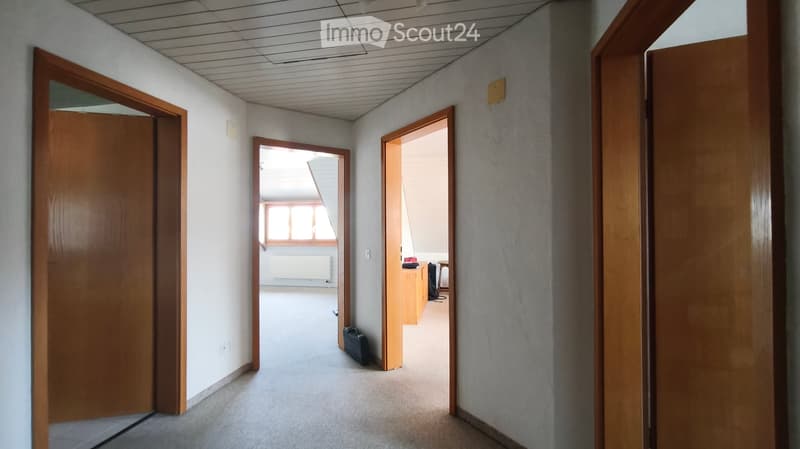 Empty hallway with multiple open wooden doors leading to rooms, carpeted floor, and white walls.