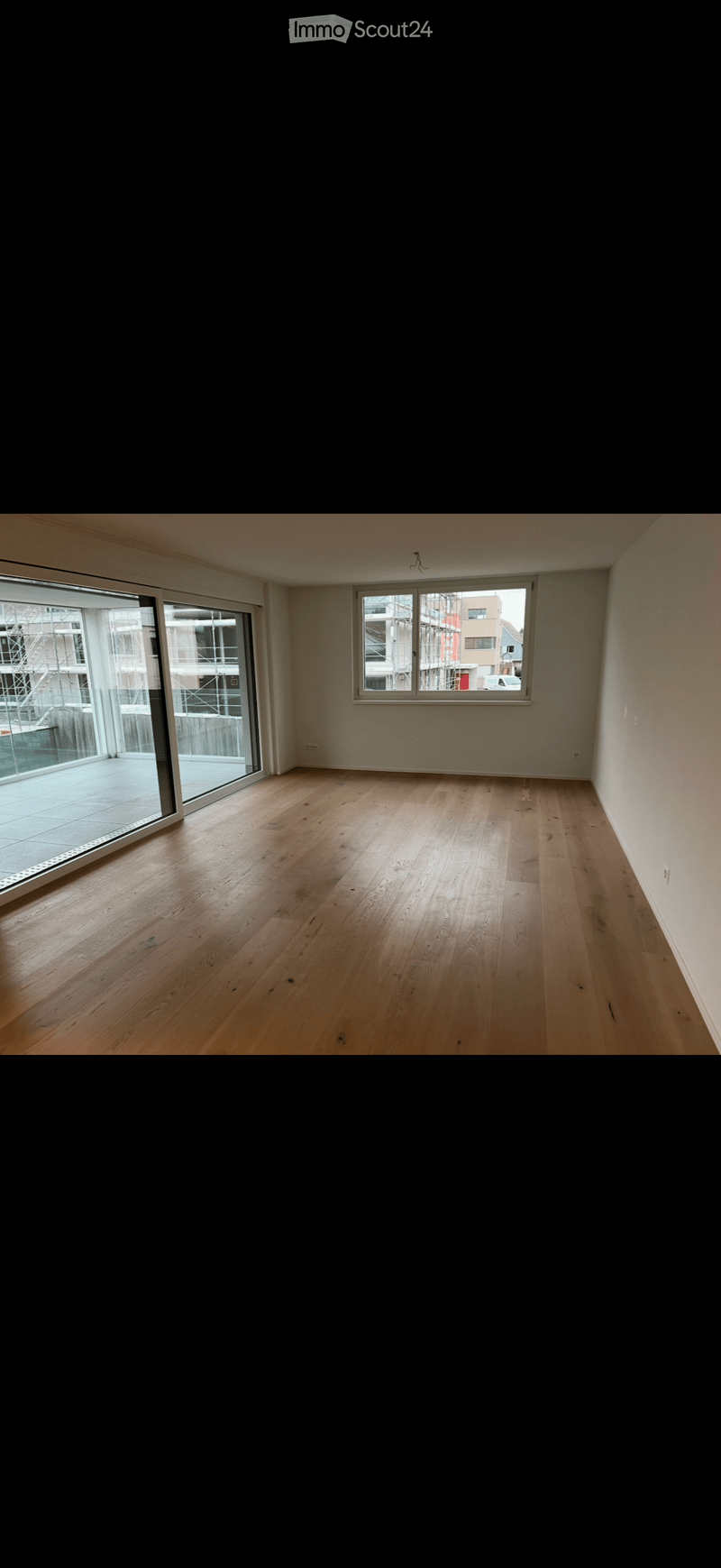 Empty room with wooden flooring, large sliding glass door, and a window showing a view of construction.