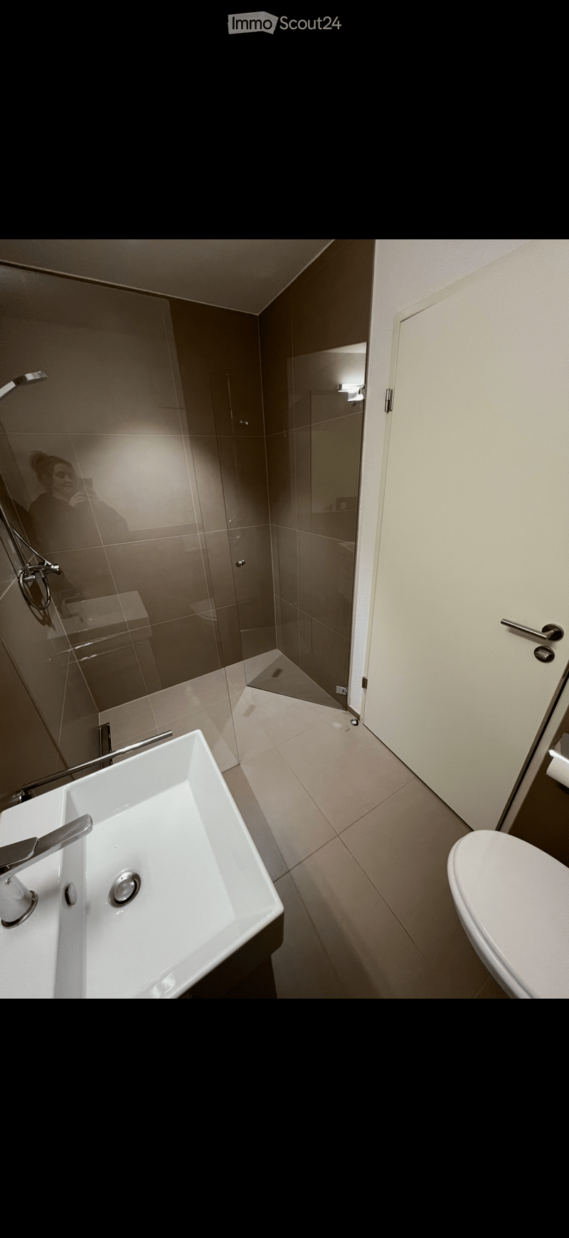 Modern bathroom with a white sink, chrome faucet, toilet, and glass-enclosed shower area.