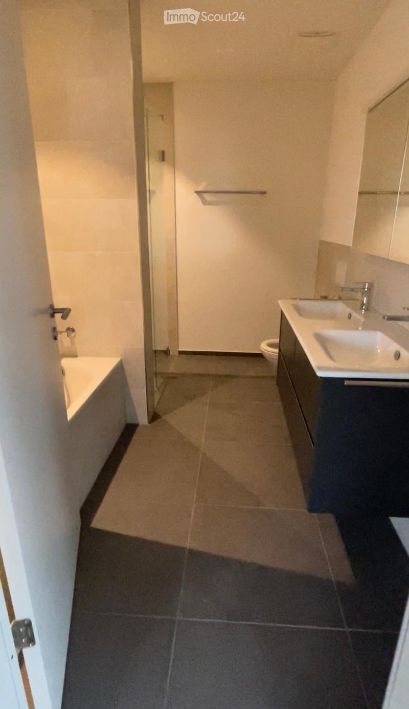 Modern bathroom with dark tiled floor, white bathtub, toilet, and double sink with chrome faucets. Features a glass shower enclosure and a towel rack.