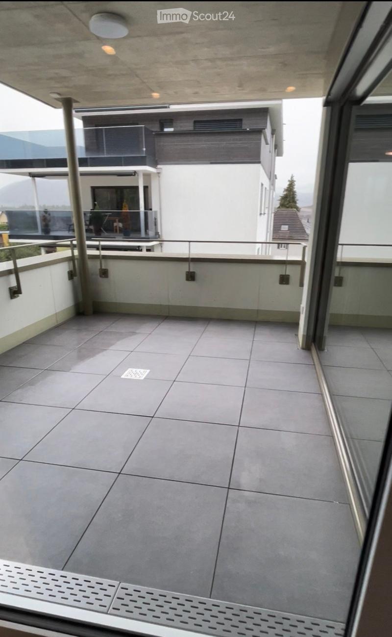 Modern balcony with tiled floor, metal railing, and a view of a contemporary building in the background.