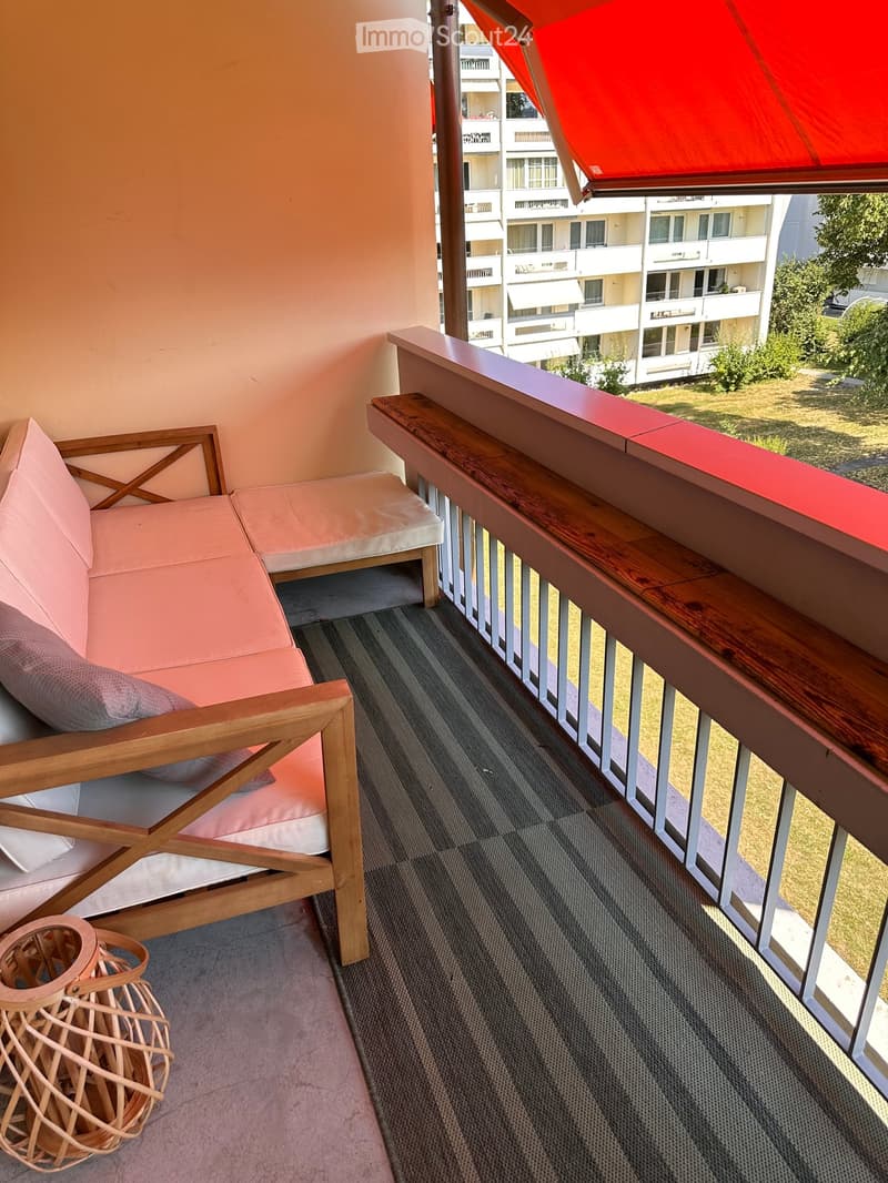 Balcony with a wooden railing, a pink sofa, a matching chair, and a small wicker table.