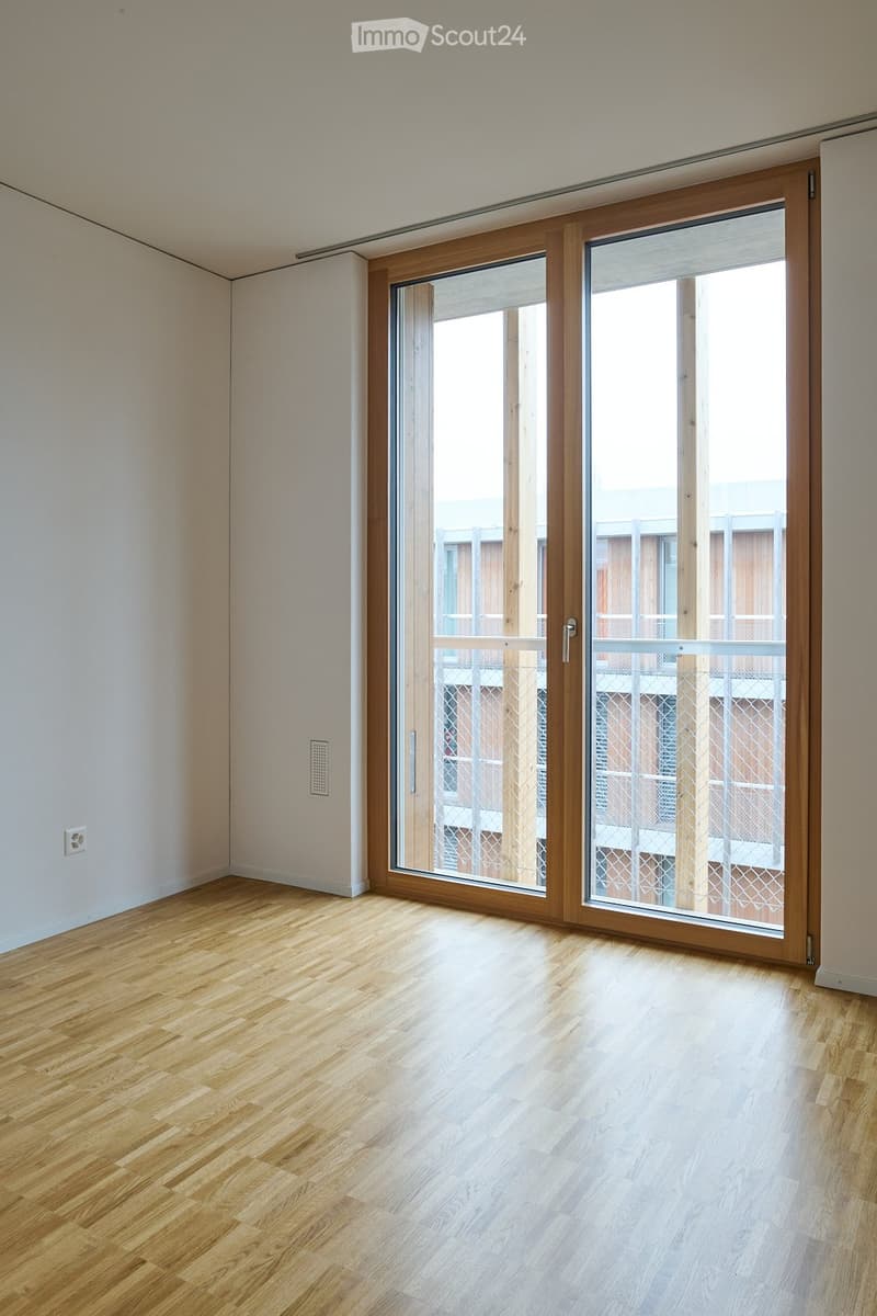 Empty room with wooden flooring, white walls, and large sliding glass doors leading to a balcony.
