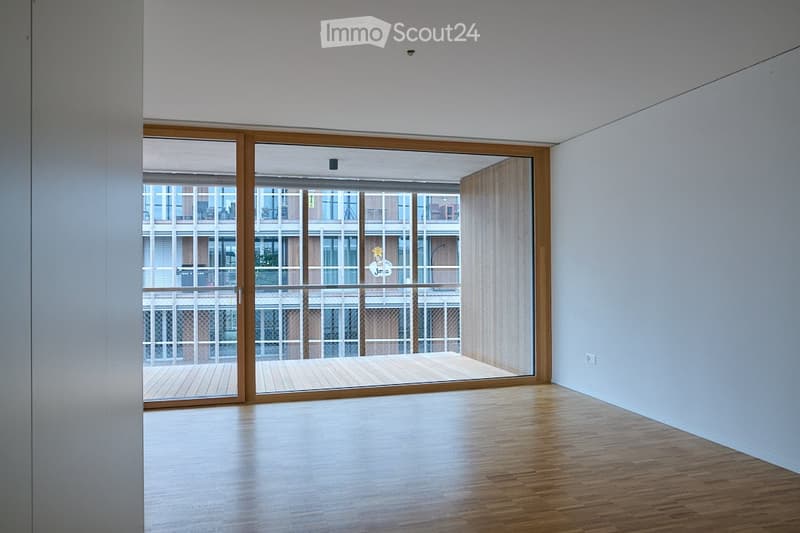 Empty room with wooden flooring, large sliding glass doors leading to a balcony, white walls, and modern lighting fixture.