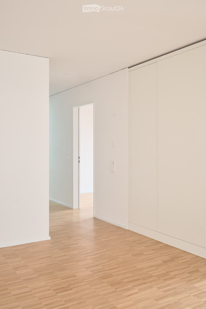 Empty room with light-colored walls, wooden flooring, and a doorway leading to another space.