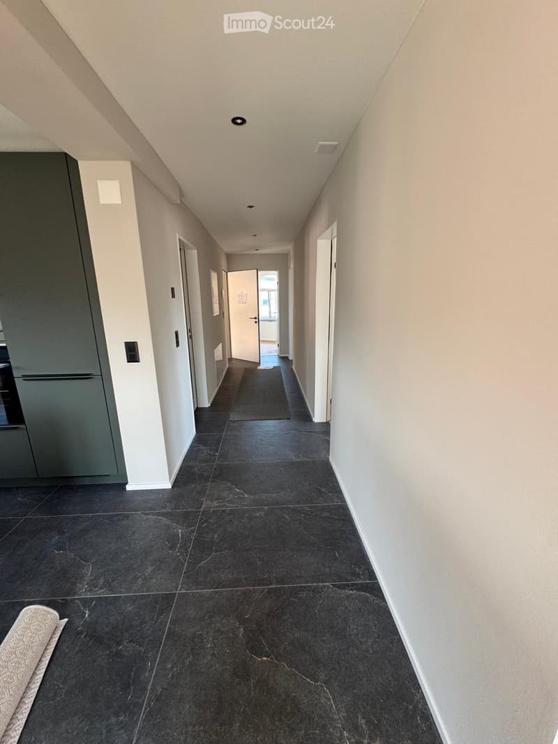 Clean, modern hallway with dark tiled flooring, white walls, and several doors leading to different rooms.