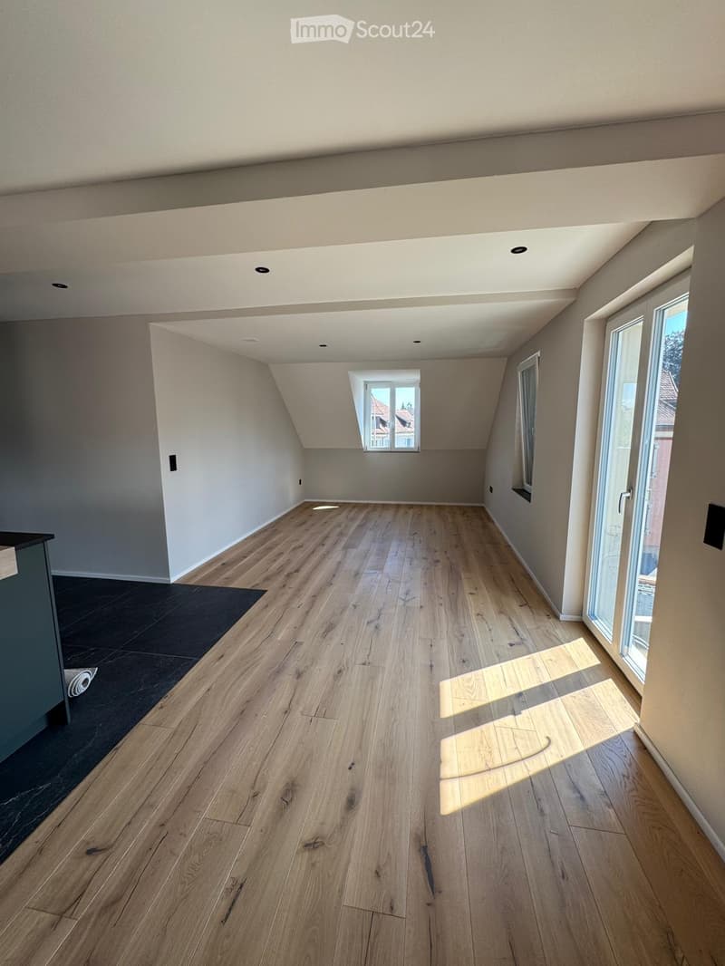 Empty room with wooden flooring, large windows, and exposed beams on the ceiling. No furniture or equipment present.