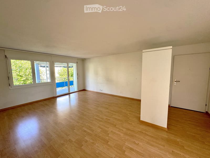 Empty room with wooden flooring, white walls, and large windows with sliding glass doors leading to a balcony.