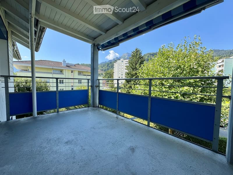 Balcony with metal railings, blue privacy screens, and a view of trees and buildings.