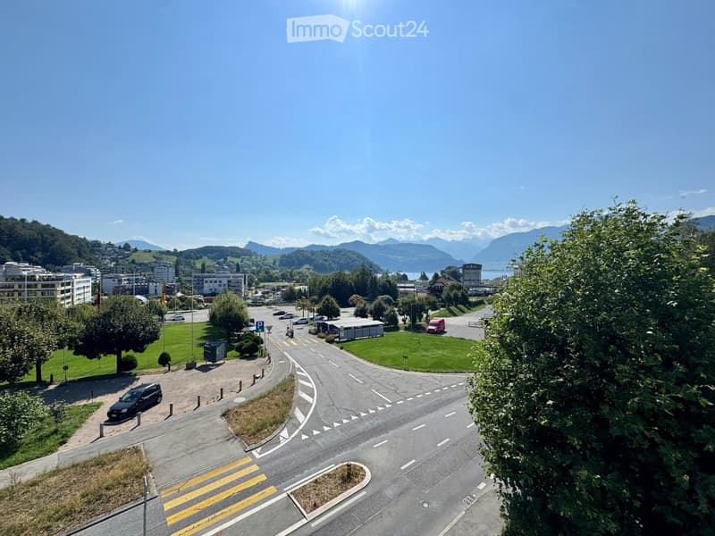 Aerial view of a suburban area with roads, parking lots, buildings, and surrounding greenery with mountains in the background.