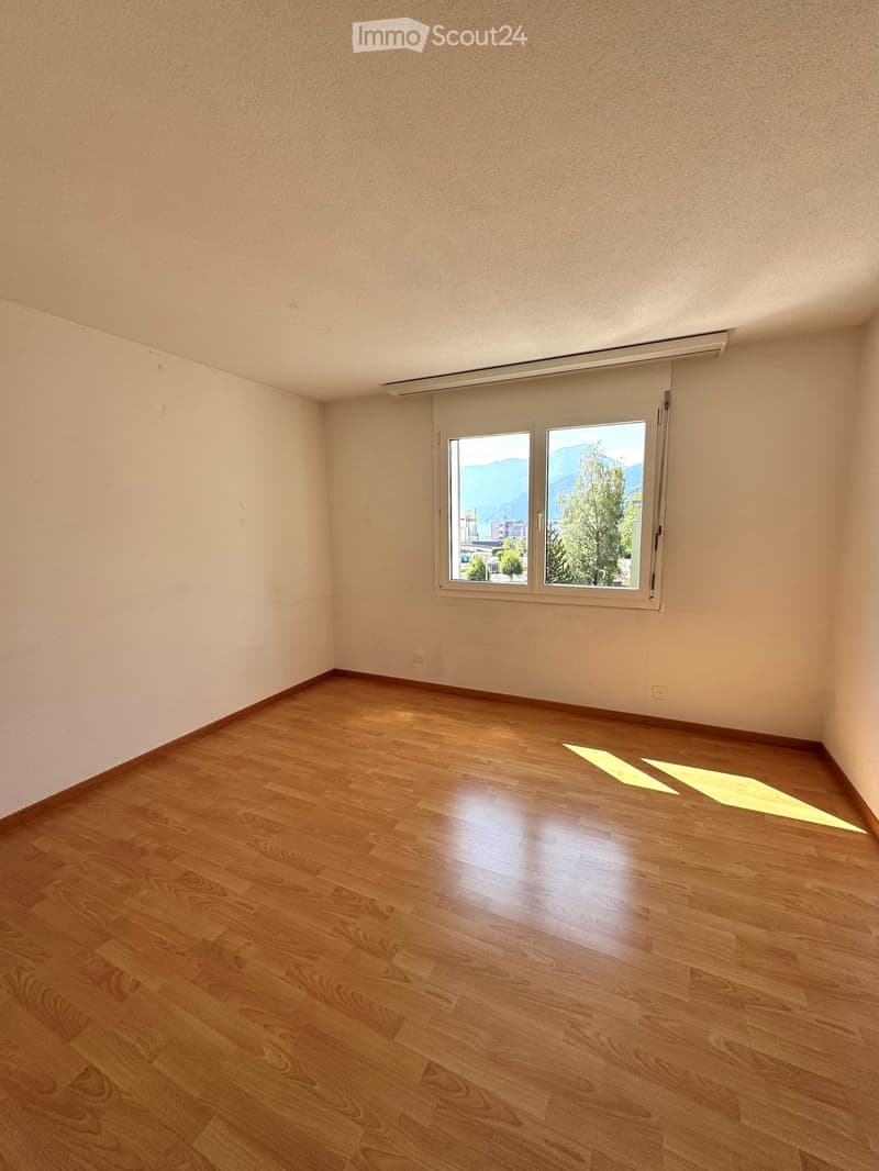 Empty room with wooden flooring and large window offering a view of mountains and trees.