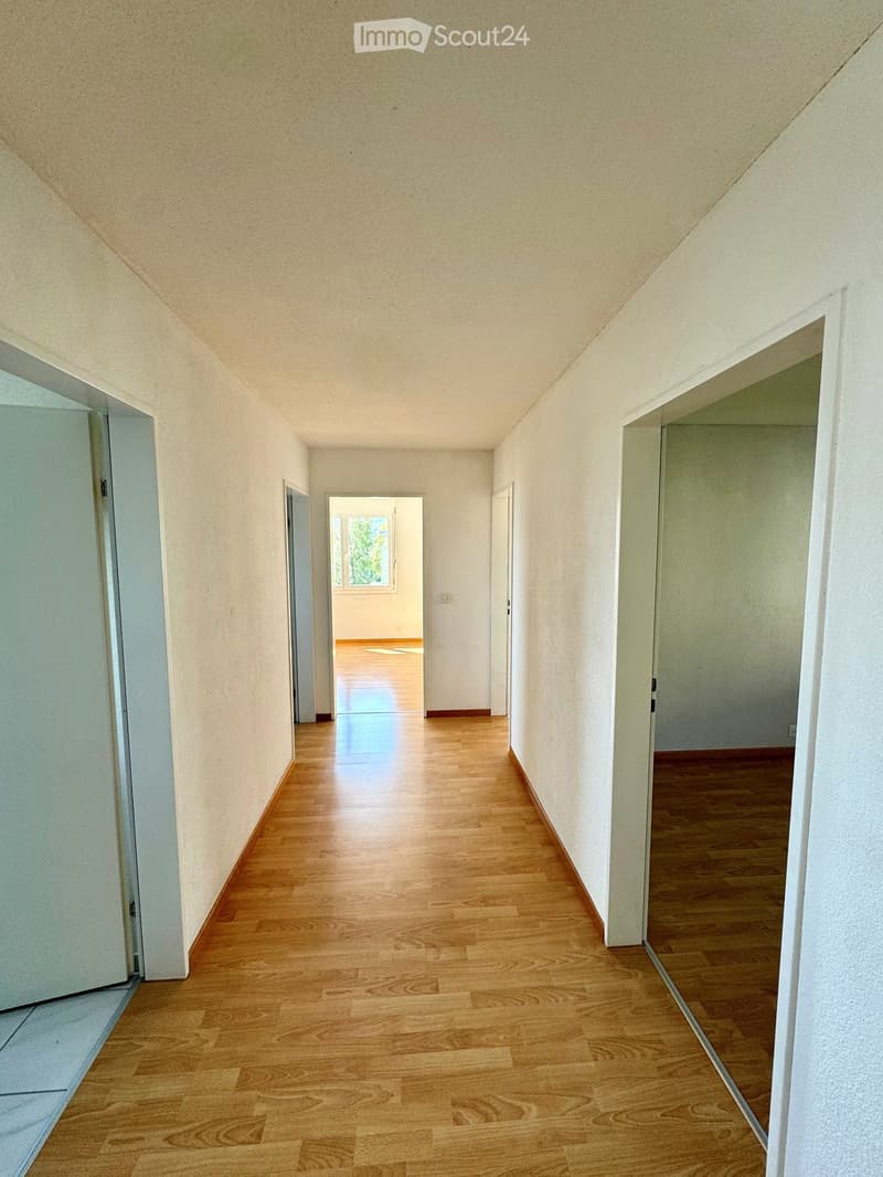 Empty hallway with wooden flooring, white walls, and several doors leading to other rooms.