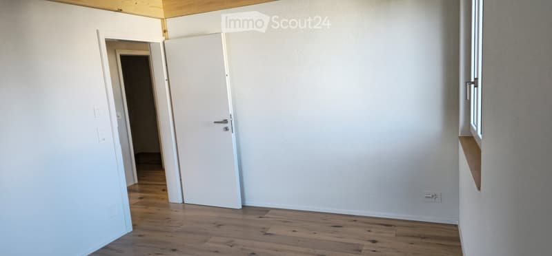 Unfurnished Room. Empty room with white walls, wooden flooring, and a white door leading to another room.