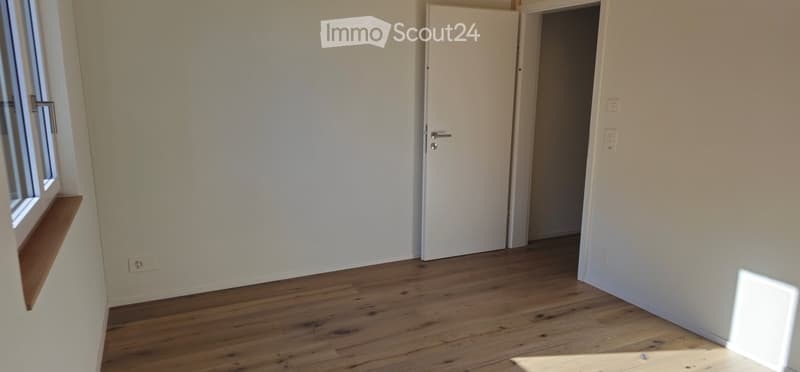 Unfurnished Room. Empty room with wooden flooring, white walls, a window with a wooden sill, and a closed white door leading to another space.