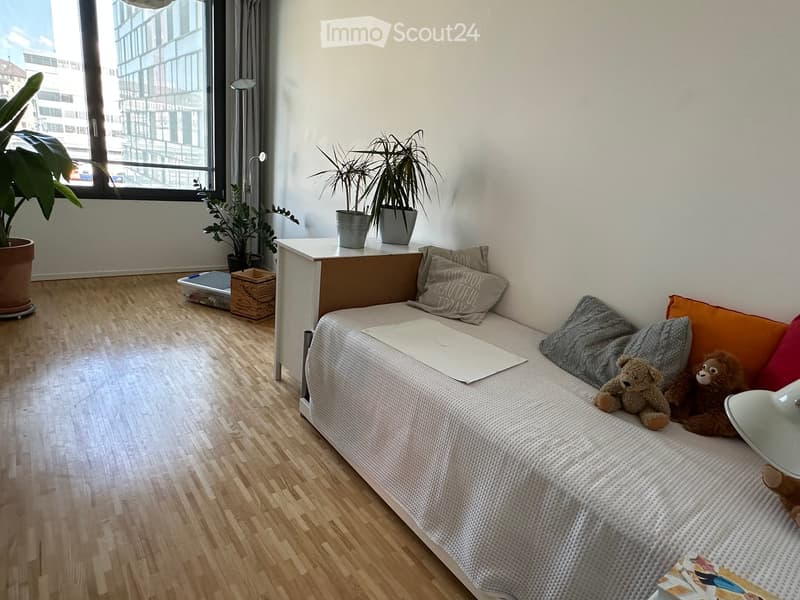 Cozy bedroom with a small sofa, decorative pillows, teddy bears, a table with potted plants, and a laptop on the sofa.