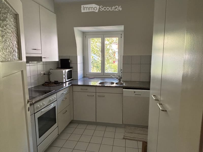 Modern kitchen with white cabinets, stainless steel appliances, tiled floor, and a window overlooking greenery.
