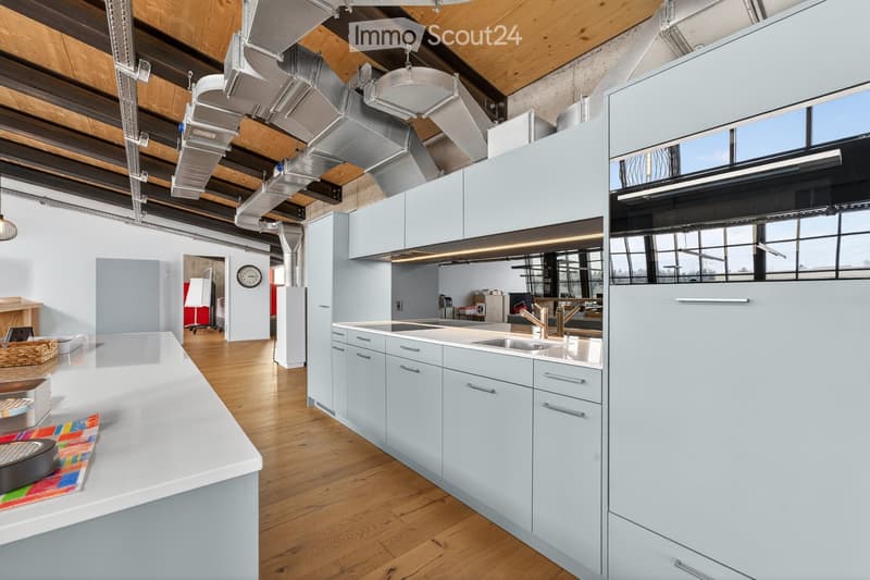 Modern kitchen with light blue cabinets, stainless steel sink, and wooden flooring. Features a large island with a white countertop, a clock on the wall, and a basket on the floor.