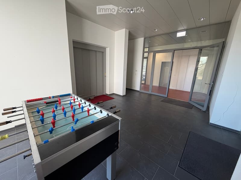 Modern, minimalist room with a foosball table, dark tiled floor, white walls, and glass doors leading to another area.