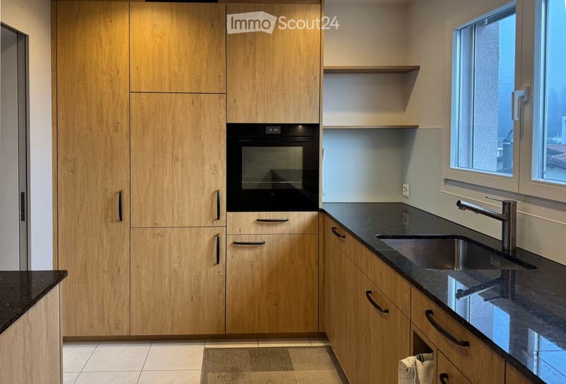 Modern kitchen with light wooden cabinets, black granite countertops, stainless steel sink and faucet, and built-in oven.