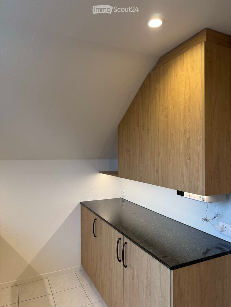 Modern kitchen with wooden cabinets, black countertop, and built-in range hood under a sloped ceiling.