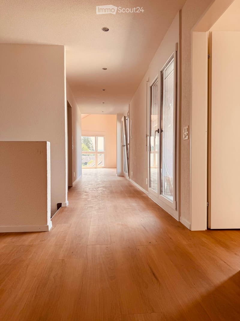 Bright hallway with wooden flooring, white walls, and recessed lighting. Features several doors and large windows allowing natural light to enter.