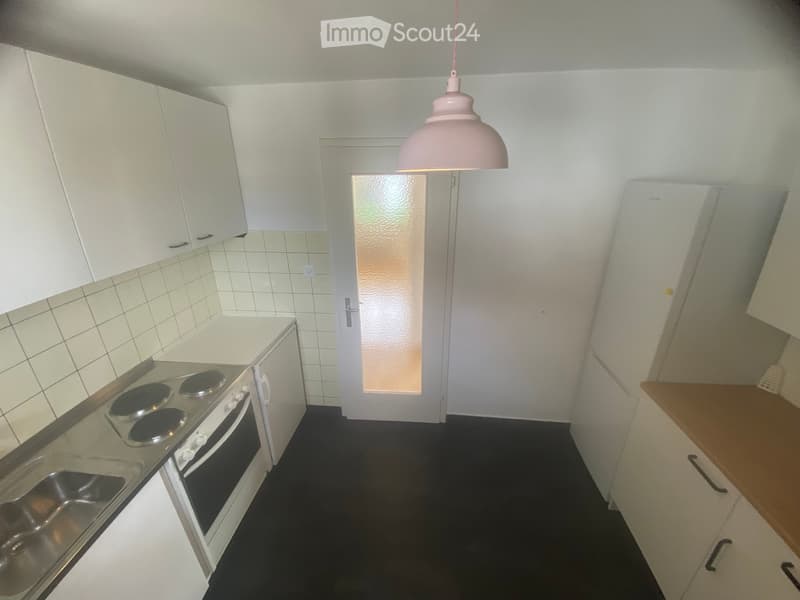 Modern kitchen with white cabinets, a four-burner electric stove, a stainless steel sink, and a pink pendant light hanging from the ceiling.