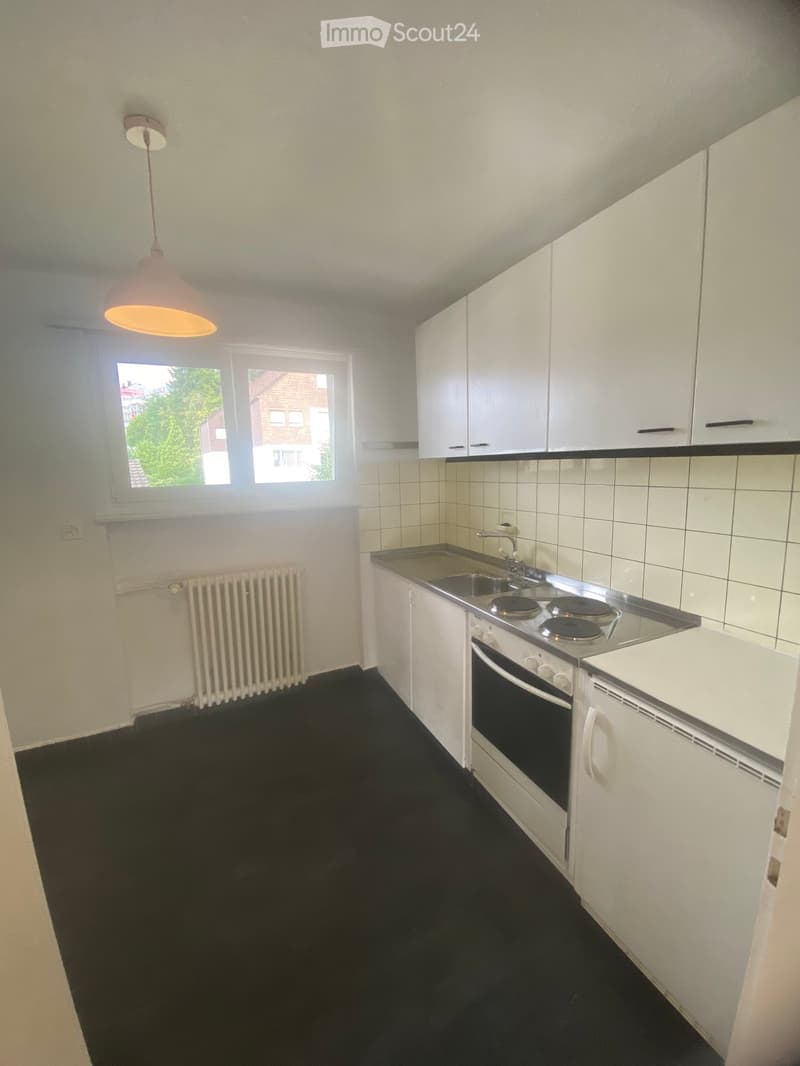 Modern kitchen with white cabinets, stainless steel sink, electric stove, and built-in oven. Features a black tiled backsplash, black floor, and a window with a view of greenery.