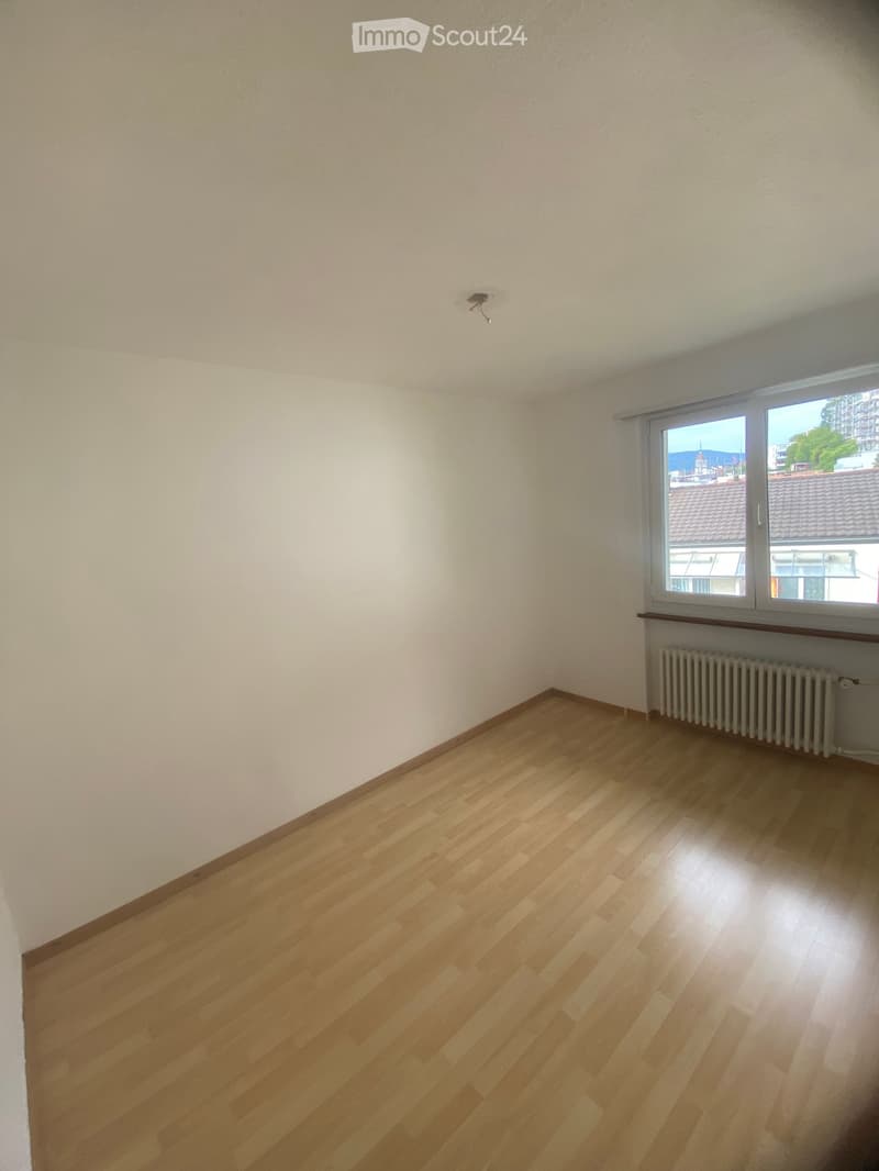 Empty room with wooden flooring, white walls, and a window with a radiator below it.
