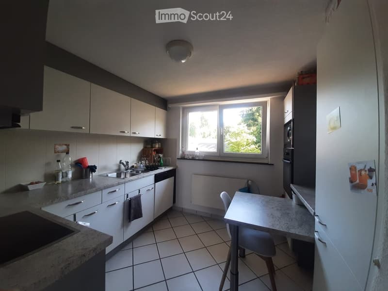 Modern kitchen with white cabinets, granite countertops, stainless steel sink, dishwasher, refrigerator, microwave, and a small dining table with a chair.