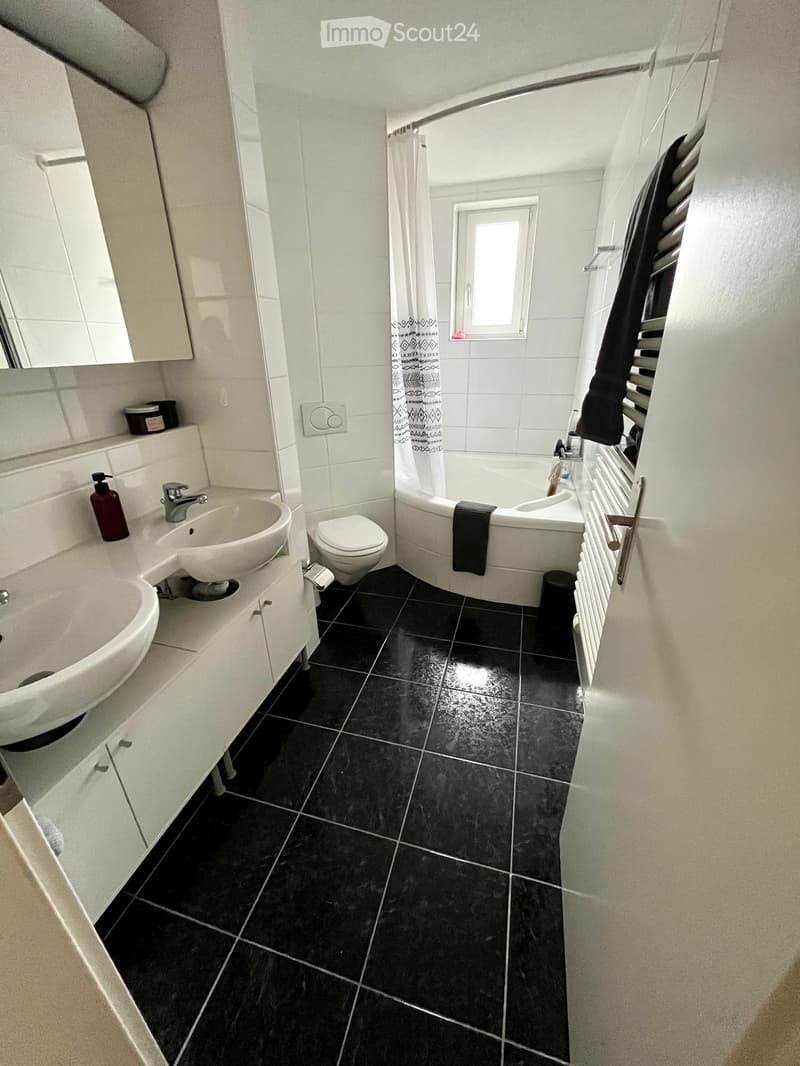 Modern bathroom with black tiled floor, white walls, sink, toilet, bathtub, radiator, and mirror.