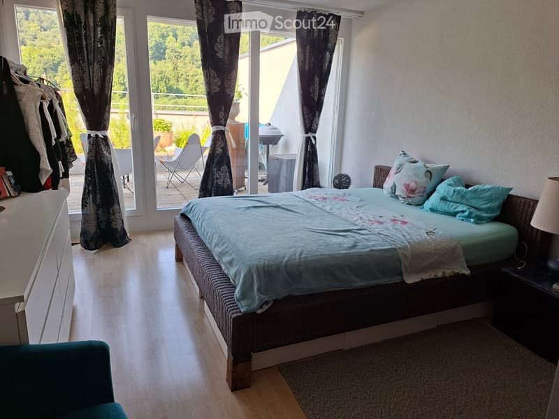 Bright bedroom with a large bed, nightstand, lamp, and a view of a balcony area with outdoor furniture.