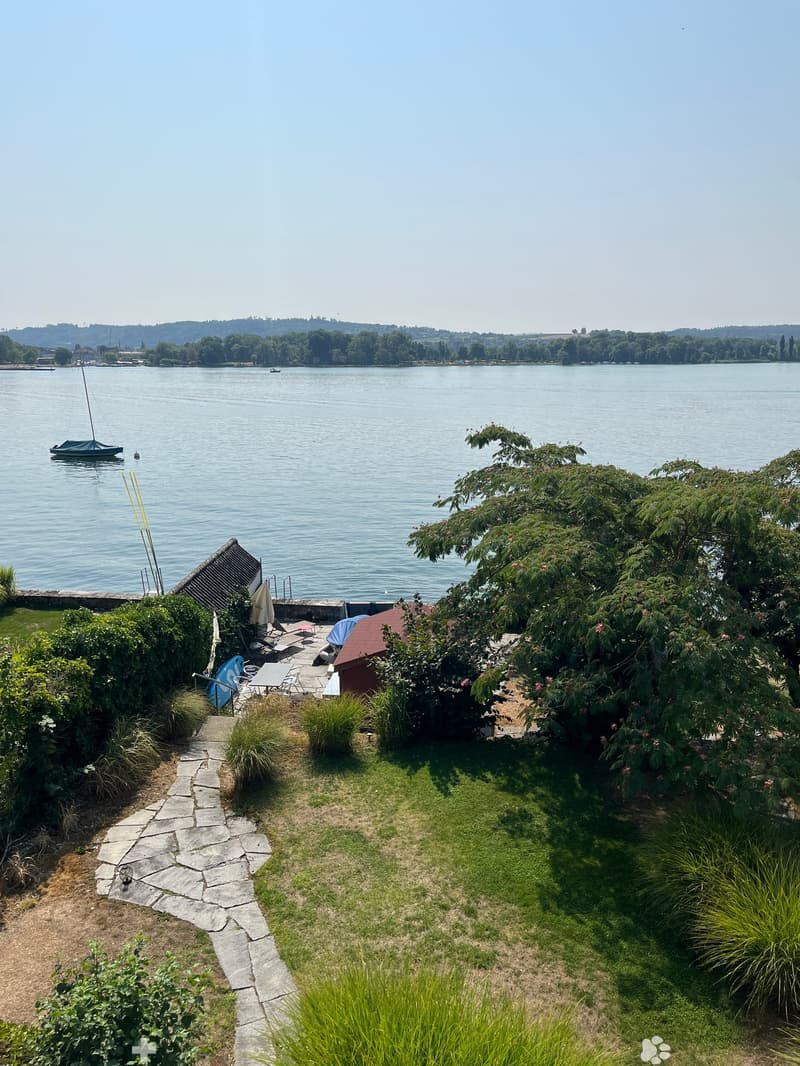 Garden area with a stone pathway, lawn, patio furniture, and a view of a lake with sailboats.