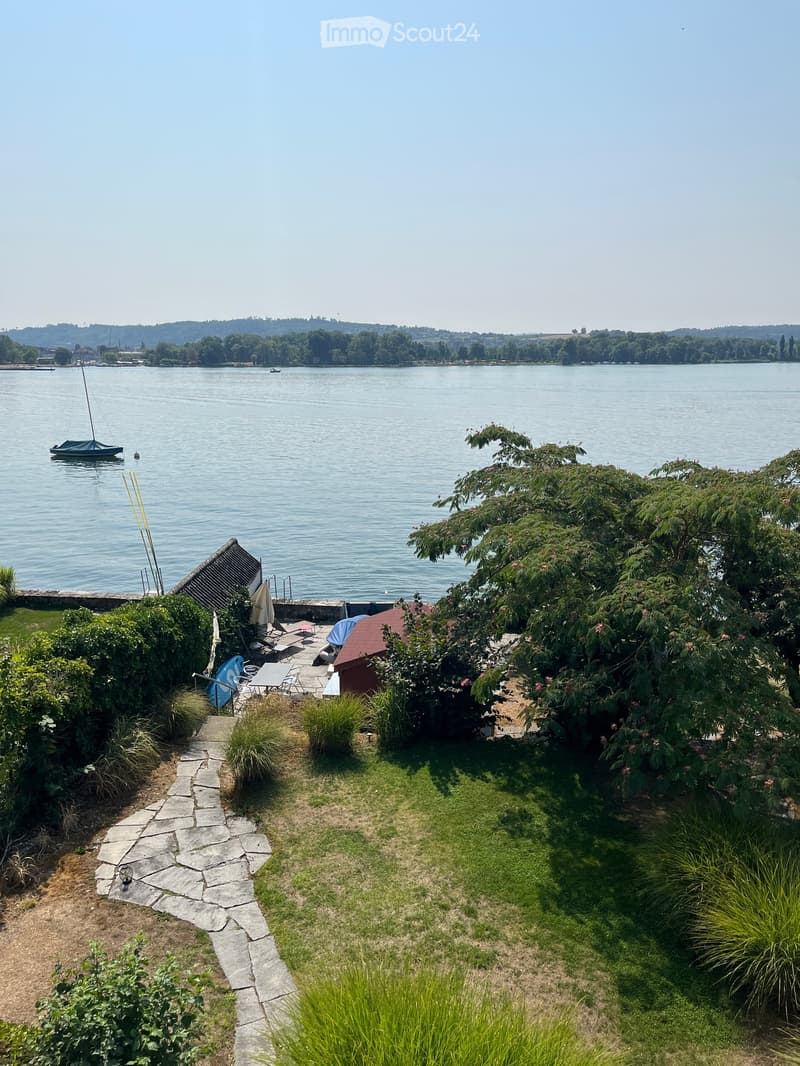 Garden area with a stone pathway, lawn, patio furniture, and a view of a lake with sailboats.