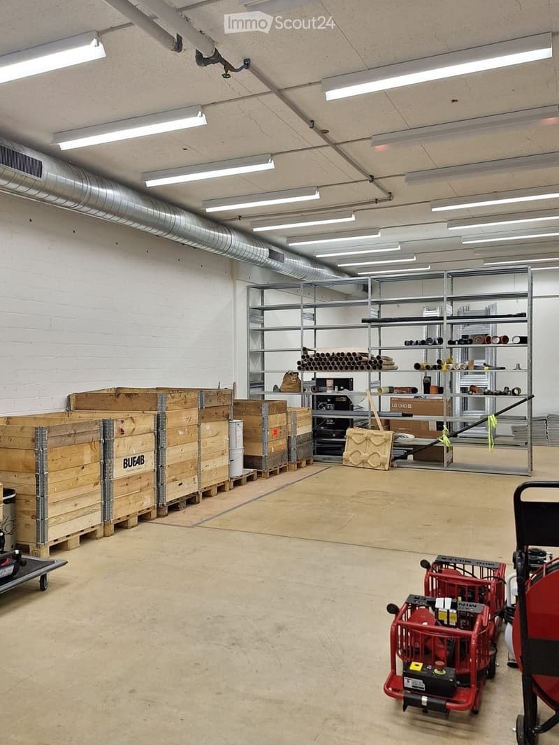 Empty warehouse space with concrete floor, exposed brick wall, metal shelving units, and storage boxes.