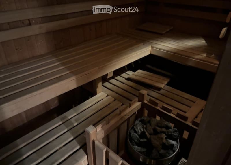 Wooden benches and slats in a sauna, with a stone bucket filled with rocks.