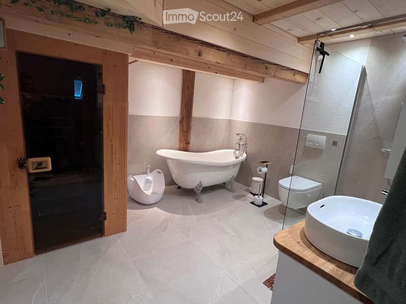 Modern bathroom with a freestanding bathtub, toilet, sink, and shower area. Features exposed wooden beams and a sleek, contemporary design.