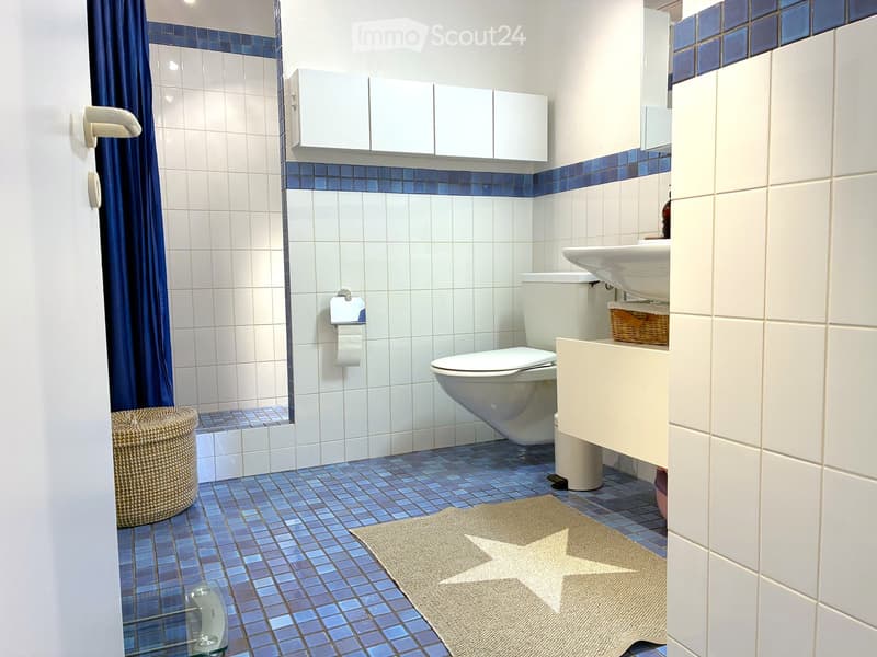 Bathroom with white tiles, blue accents, toilet, sink, and wicker baskets.