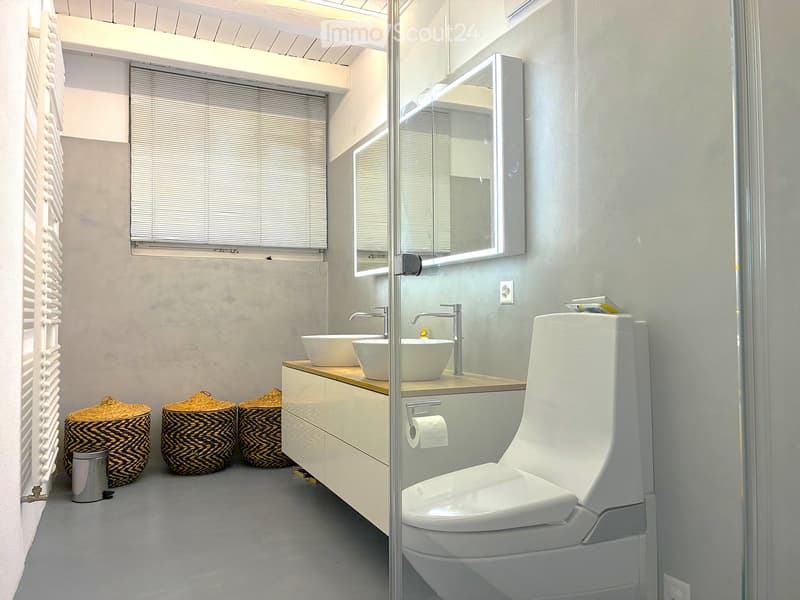 Modern bathroom with double sink vanity, toilet, large mirror, wicker baskets, and a window with blinds.