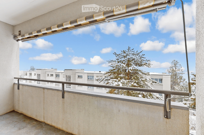 Balcony with a view of a snowy landscape, featuring a retractable awning and metal railing.