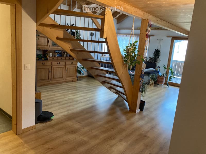 Open hallway with wooden flooring, staircase leading to an upper level, visible cabinets, and potted plants.