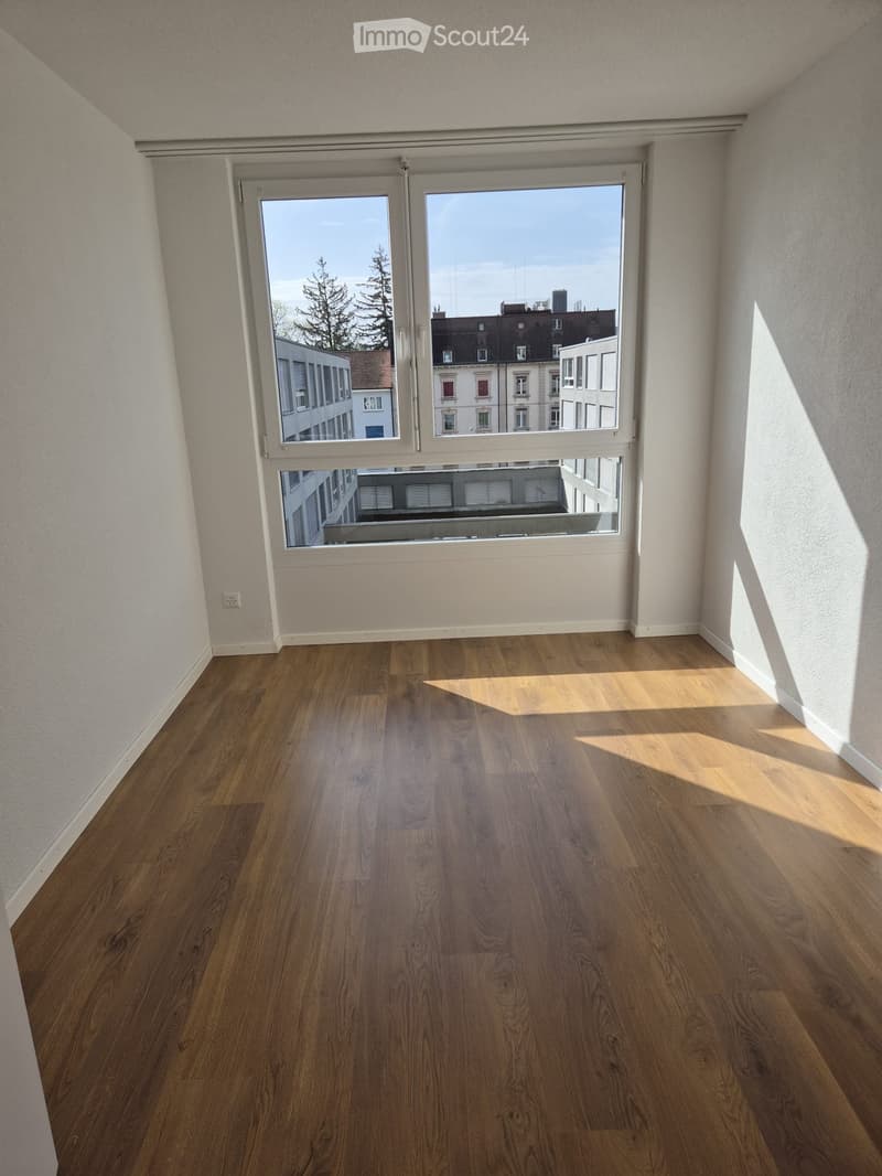 Empty room with wooden flooring and large windows offering a view of the cityscape.